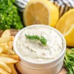 Homemade tartar sauce garnished with a sprig of dill in a white serving bowl with lemon wedges on the side