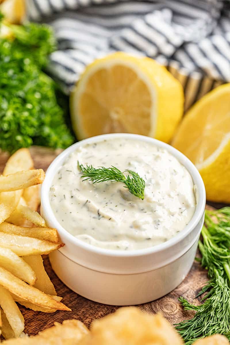 Homemade tartar sauce garnished with a sprig of dill in a white serving bowl with lemon wedges on the side
