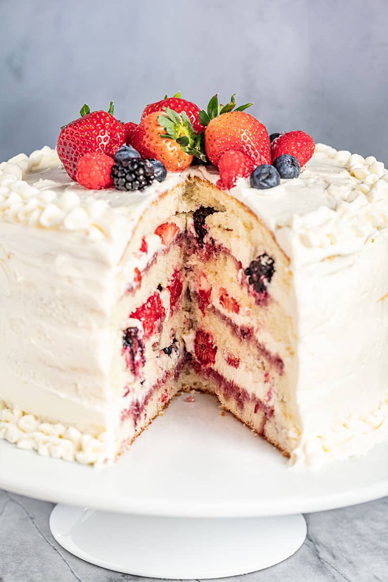 A slice missing from a whole fresh berry Chantilly cake on a cake stand