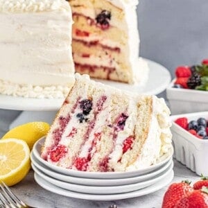A slice of fresh berry Chantilly cake on its side on a white dessert plate.