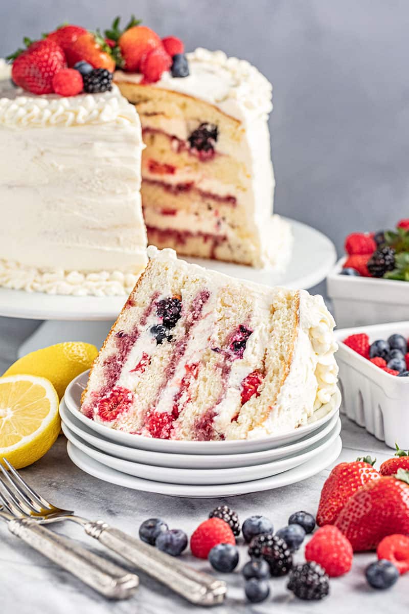 A slice of fresh berry Chantilly cake on its side on a white dessert plate.