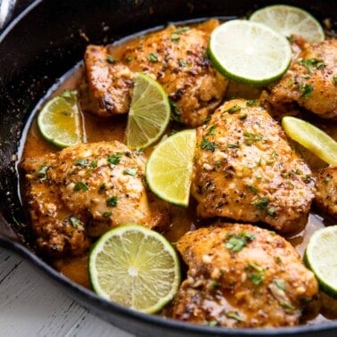 Garlic lime chicken in a skillet topped with lime slices.