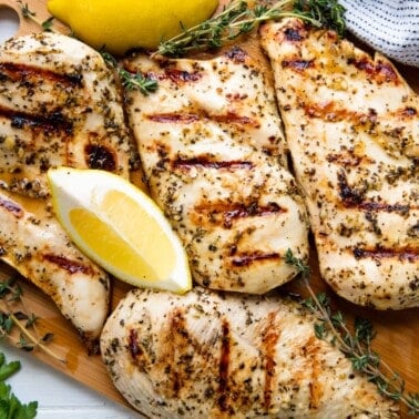 Bird's eye view of grilled chicken and lemon wedges on a cutting board.
