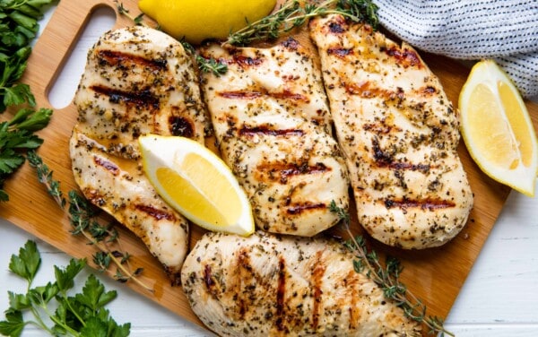 Bird's eye view of grilled chicken and lemon wedges on a cutting board.