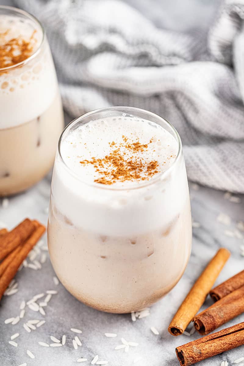 A glass of horchata with cinnamon sticks surrounding it