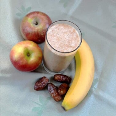 Overhead view of an apple pie smoothie surrounded by apples, dates, and a banana