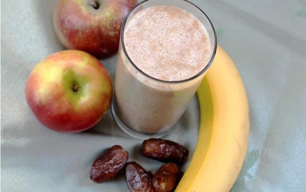 Overhead view of an apple pie smoothie surrounded by apples, dates, and a banana
