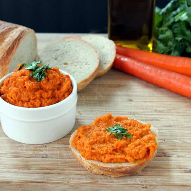 Slice of bread on a cutting board with carrot spread on top and a bowl of carrot spread in the background