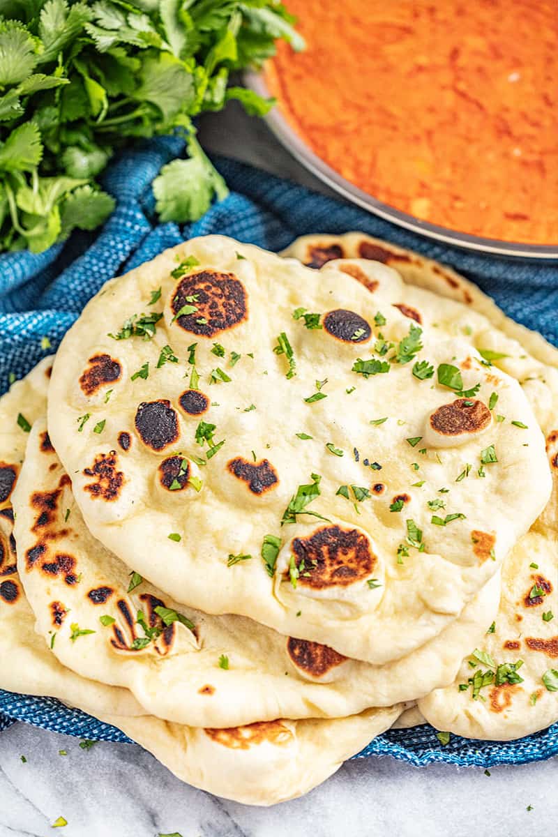 Stack of charred naan bread garnished with pieces of chopped cilantro