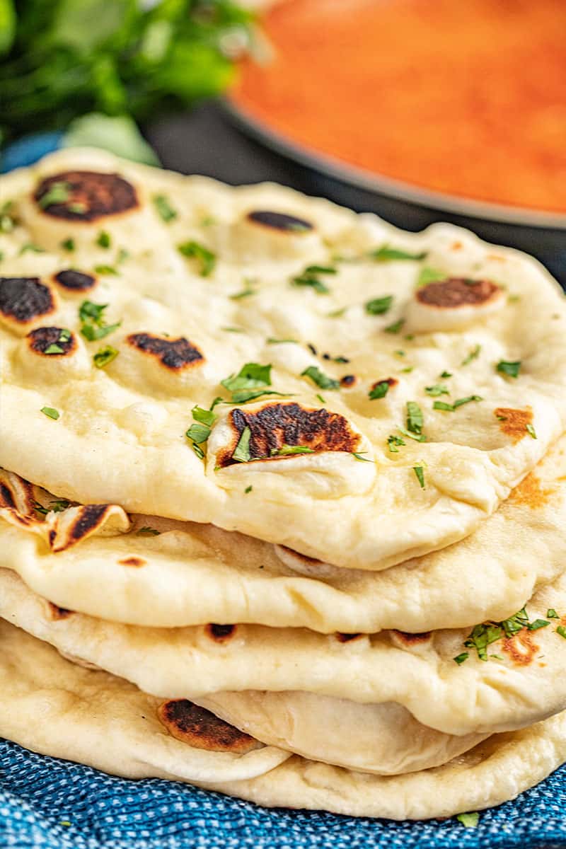 5 pieces of naan bread stacked on top of each other with a pan of tikka masala in the background