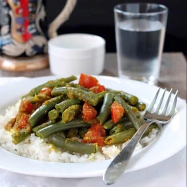 Green beans with chunks of tomato served over rice on a white plate with a fork