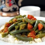 Green beans with chunks of tomato served over rice on a white plate