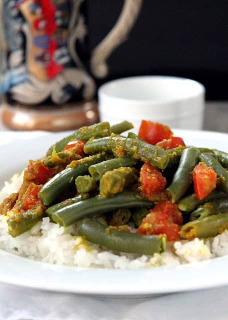 Green beans with chunks of tomato served over rice on a white plate