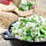 A cracker being dipped into a cast iron bowl filled with jicama salsa