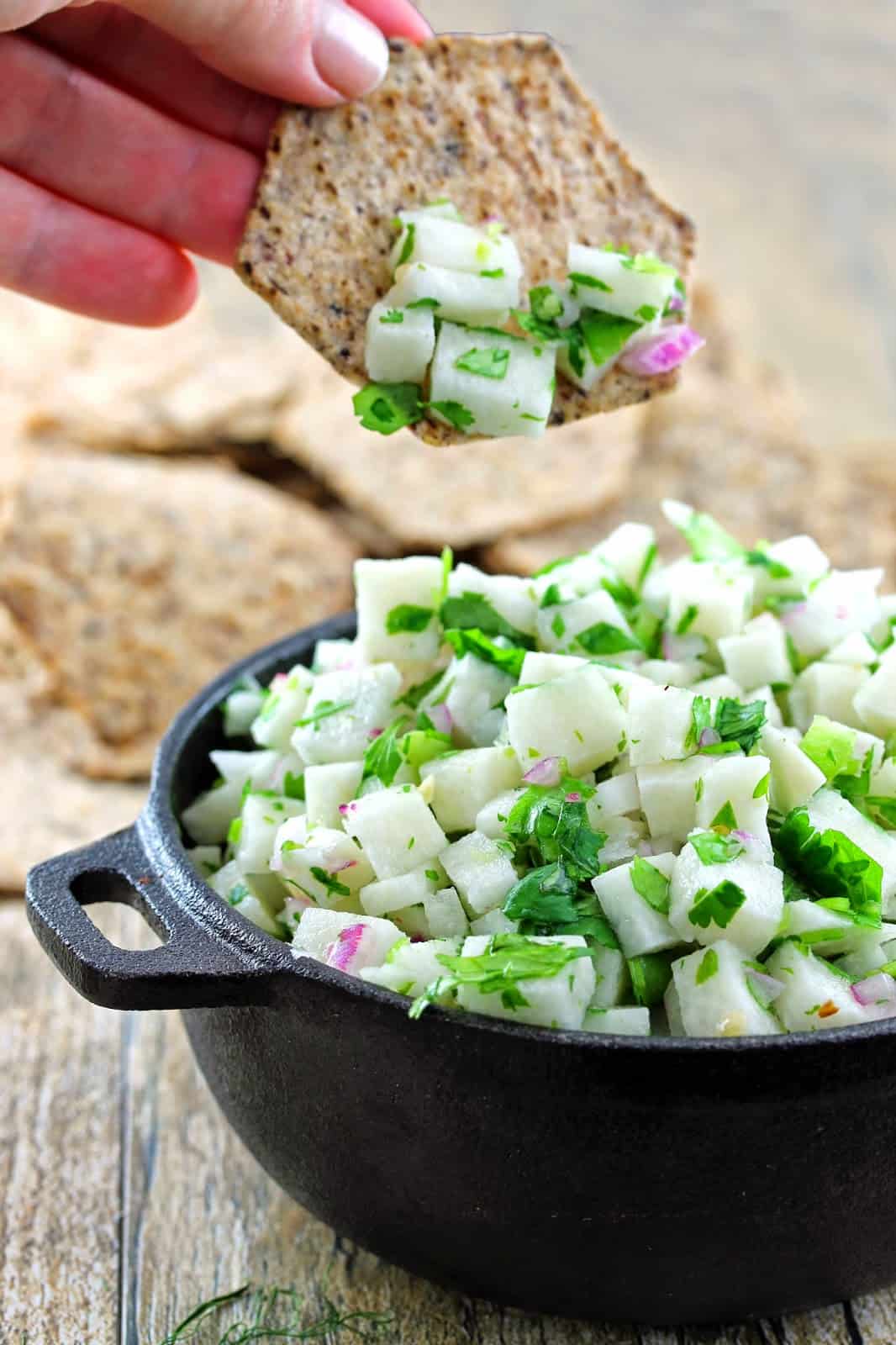 A cracker being dipped into a cast iron bowl filled with jicama salsa