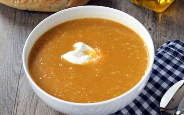 A white bowl filled with masala spiced butternut squash soup and a dollop of sour cream in the center