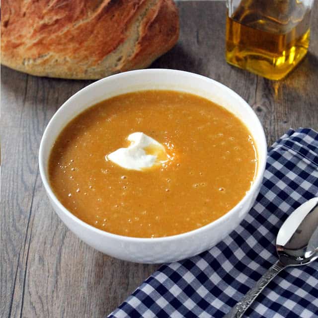 A white bowl filled with masala spiced butternut squash soup and a dollop of sour cream in the center