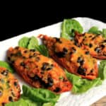 Four Mexican Stuffed Sweet Potatoes on a white plate and garnished with spinach leaves