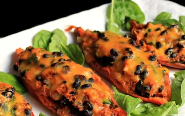 Four Mexican Stuffed Sweet Potatoes on a white plate and garnished with spinach leaves