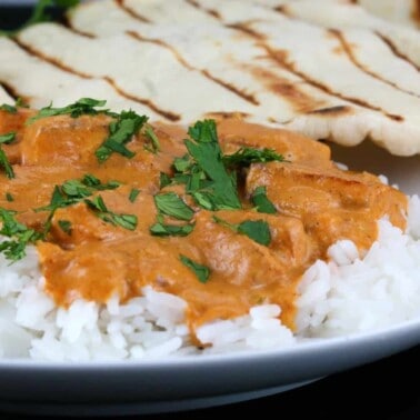 Paneer tikka masala served over white rice on a white plate with naan on the side
