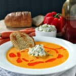 White bowl full of Red Curry Carrot Soup with a slice of bread in it.