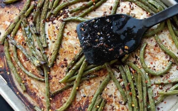 Black spatula resting on a sheet pan with roasted green beans