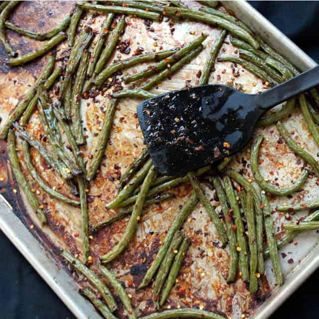 Black spatula resting on a sheet pan with roasted green beans