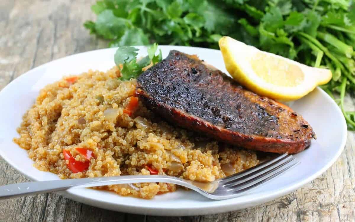 Blackened salmon portion over quinoa on a white plate with a fork resting on the plate