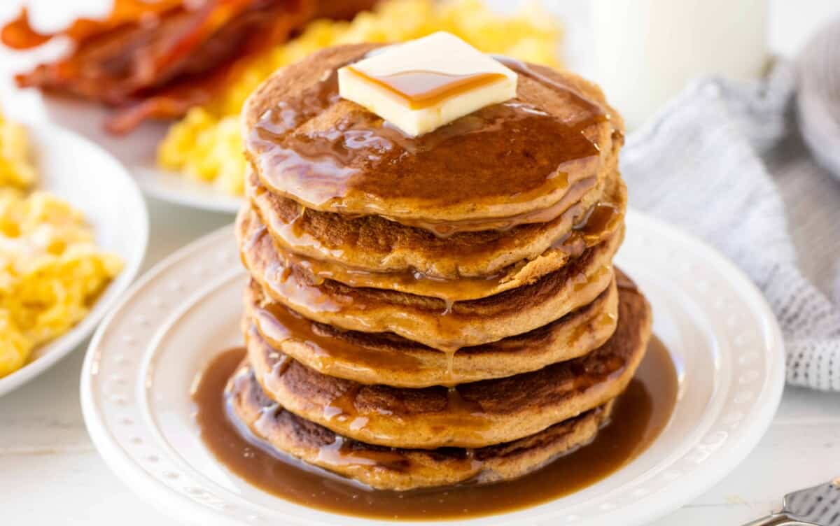 A stack of whole wheat pancakes topped with a pad of butter and syrup.