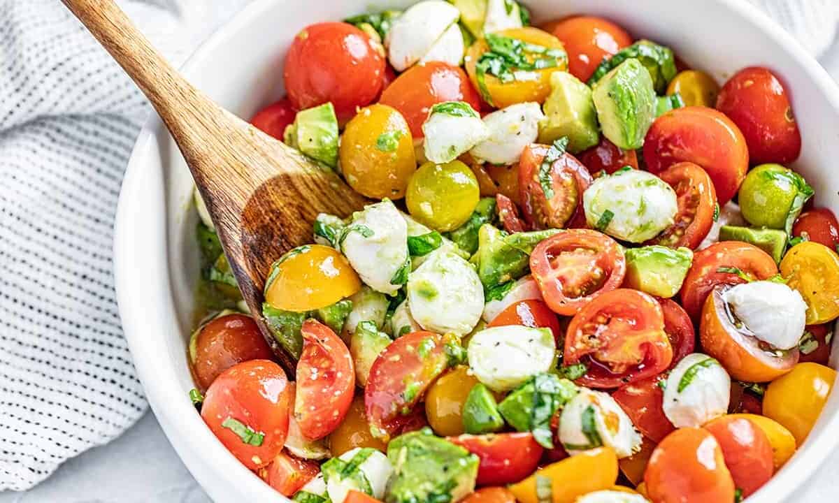 Caprese Avocado Salad in a white bowl with a wooden spoon