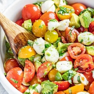 Caprese Avocado Salad in a white bowl with a wooden spoon