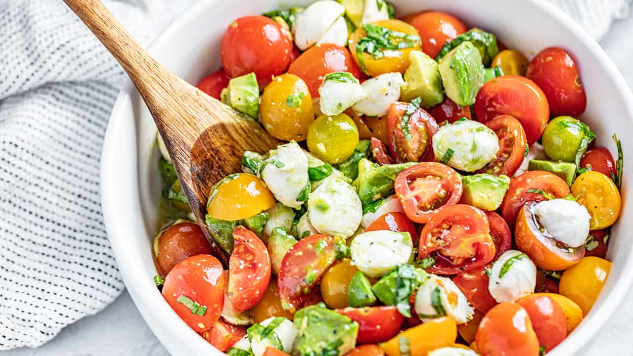 Caprese Avocado Salad in a white bowl with a wooden spoon