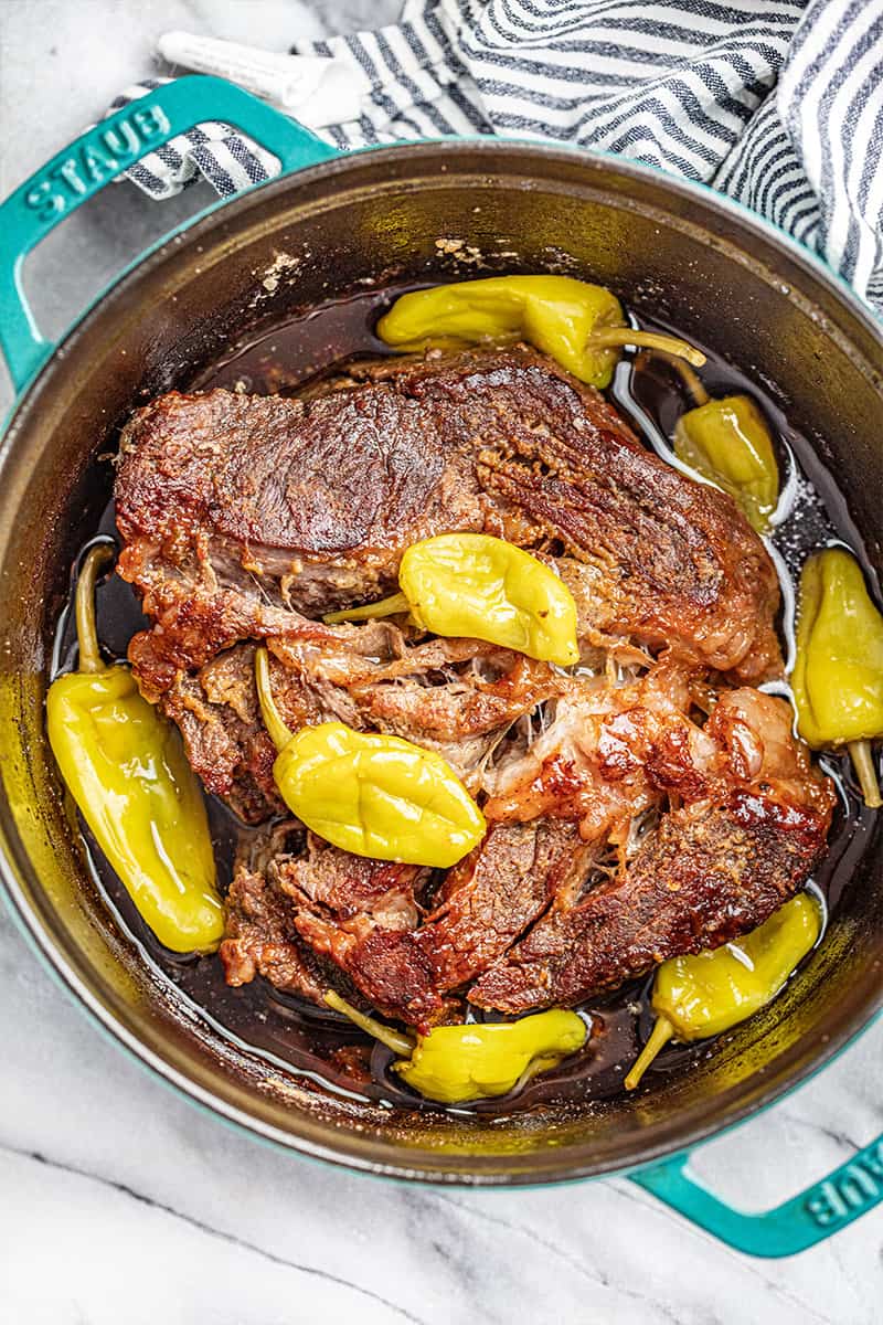 looking down into a dutch oven with a pot roast and pepperoncinis