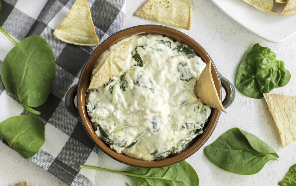 overhead view of a bowl of spinach artichoke dip with tortilla chips dunked in