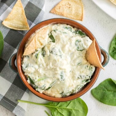 overhead view of a bowl of spinach artichoke dip with tortilla chips dunked in
