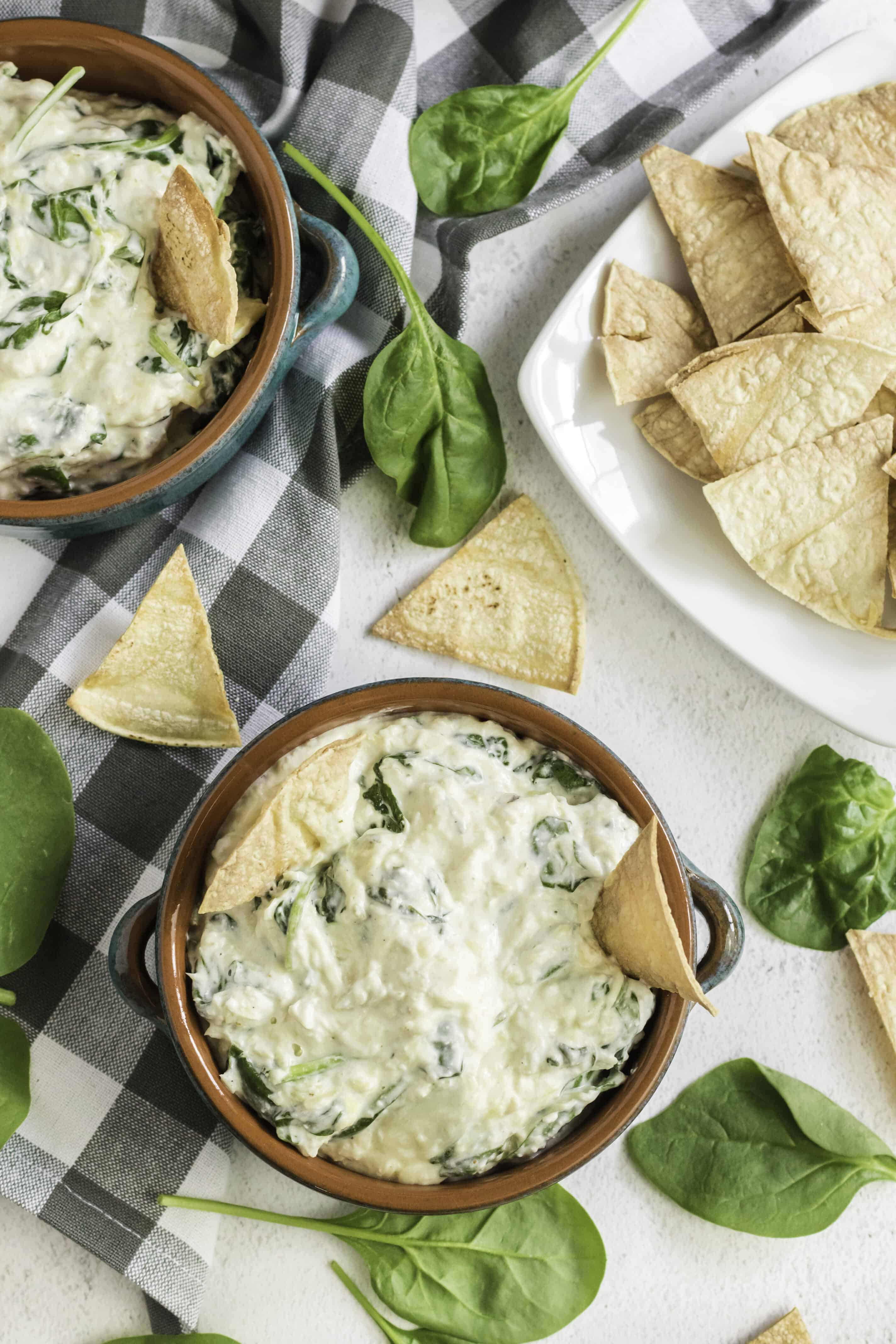 overhead shot of spinach artichoke dip in a bowl surrounded by tortilla chips and fresh spinach