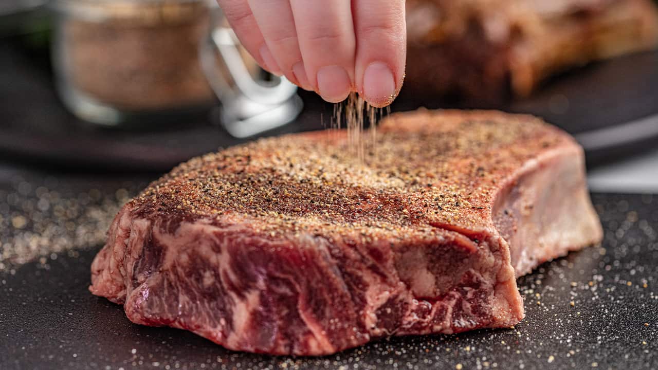 applying steak seasoning to a raw steak