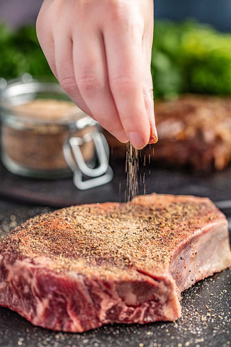sprinkling steak seasoning on top of raw steak