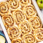 A white and red baking pan filled with 12 caramel apple cinnamon rolls