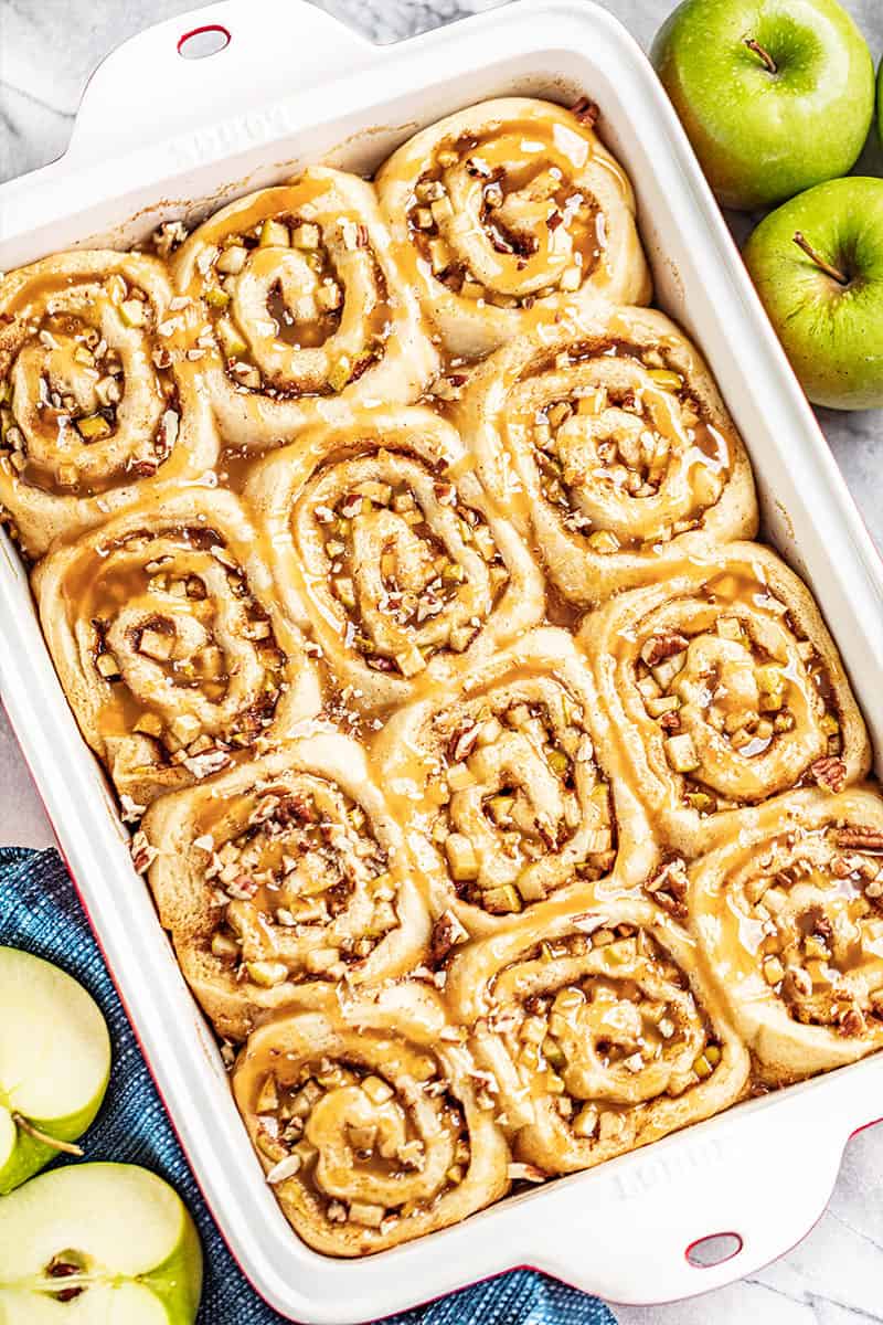 A white and red baking pan filled with 12 caramel apple cinnamon rolls