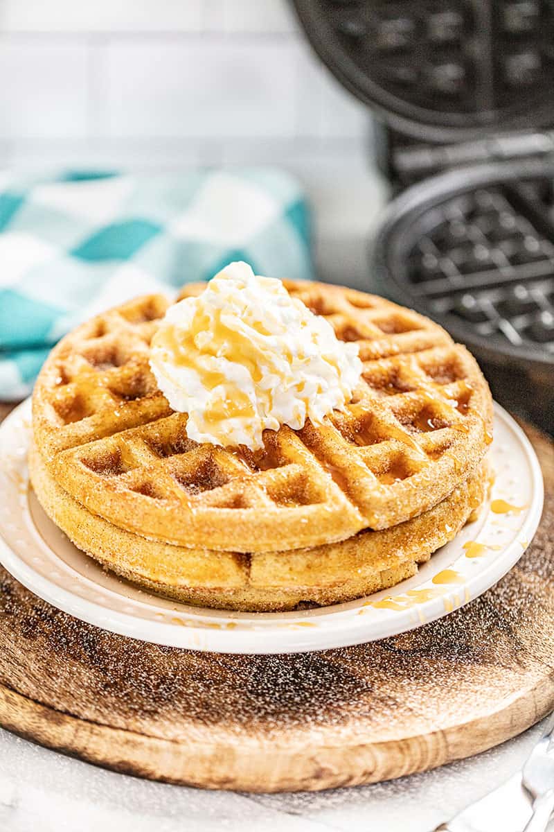 caramel churro waffles son a white plate with a spoonful of butter