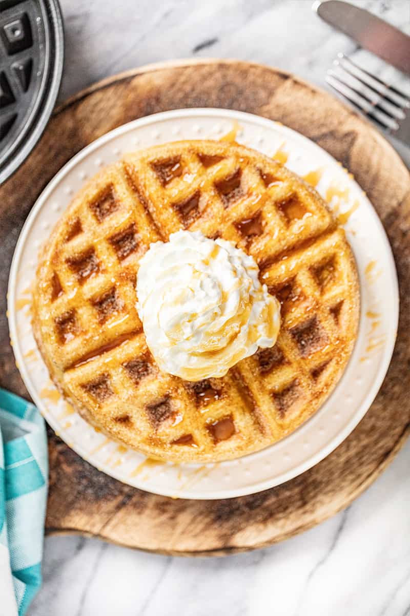overhead view of a white plate with stacked churro waffles with whipped butter and caramel on top