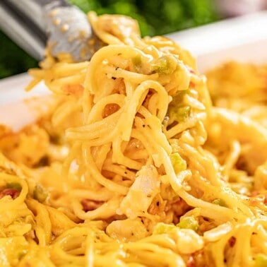 Cheesy chicken spaghetti in a baking dish with tongs serving some out