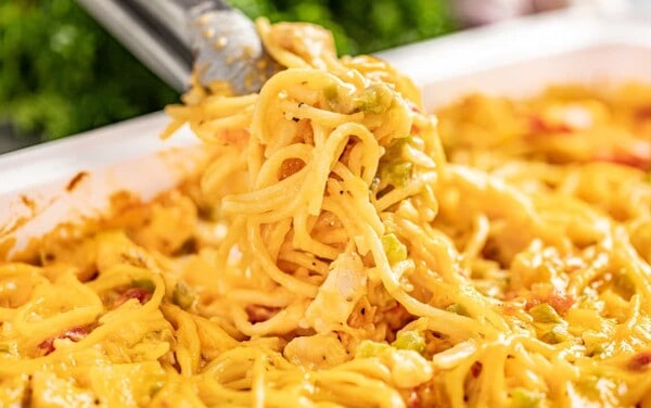 Cheesy chicken spaghetti in a baking dish with tongs serving some out