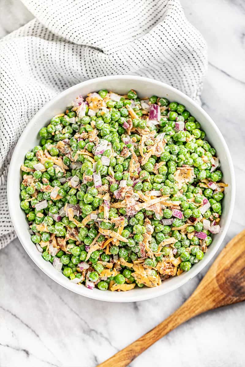 A bowl filled with pea salad with a wooden spoon next to the bowl