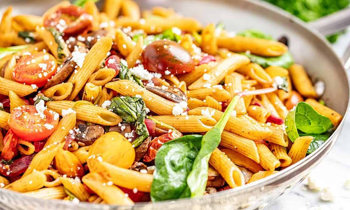 A large bowl filled with pasta, spinach, cherry tomatoes, and feta cheese