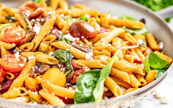A large bowl filled with pasta, spinach, cherry tomatoes, and feta cheese