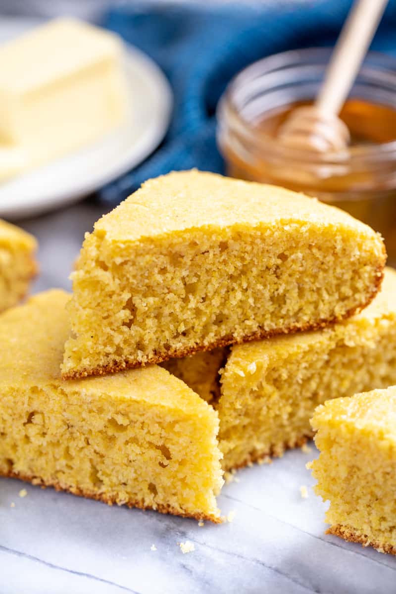 A pile of sliced cornbread with honey and butter in the background