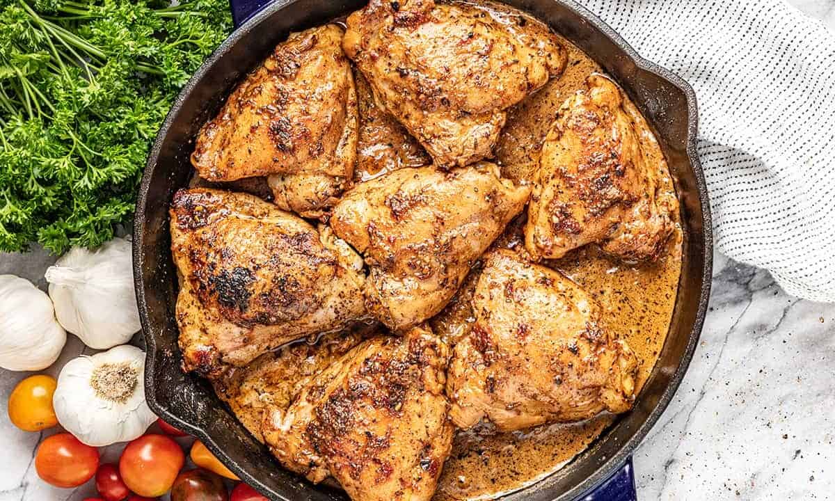 A skillet full of chicken thighs in a creamy sun dried tomato sauce