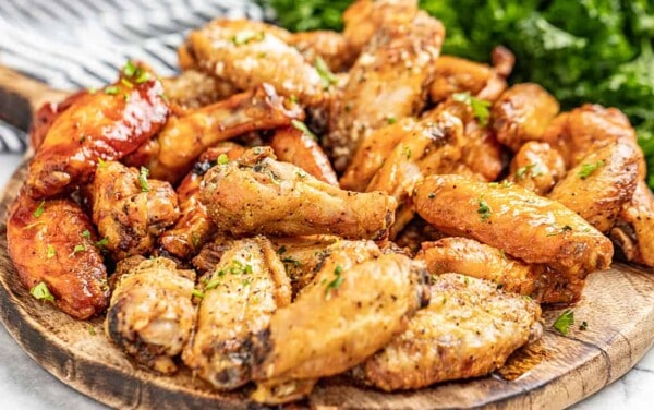 A wooden serving board filled with chicken wings, sprinkled in parsley